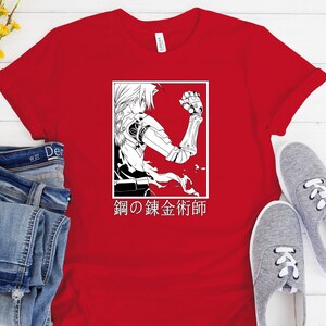 May include: Red t-shirt featuring a black and white graphic of an anime character with mechanical arm and the Japanese text "Fullmetal Alchemist" in a white rectangle. The shirt is paired with blue jeans and gray sneakers.