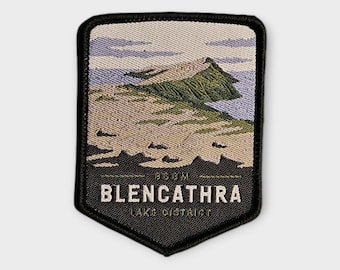 Puede incluir: Un parche bordado rectangular con un borde inferior puntiagudo que muestra el paisaje de la montaña Blencathra en el Lake District. El diseño incluye un pico verde, un primer plano beige y un cielo azul claro. El texto dice BLENCATHRA.
