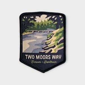 May include: A navy blue patch with a landscape design featuring a river, trees, and a bridge. The text "TWO MOORS WAY" is displayed above "Exmoor - Dartmoor". The patch has a shield shape.