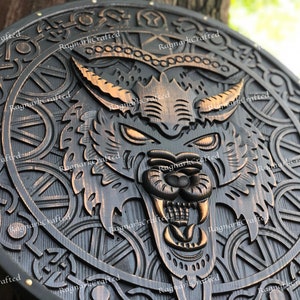 May include: A round wooden shield with a carved wolf's head in the center. The shield is decorated with intricate Celtic knotwork and has a black background with gold accents.