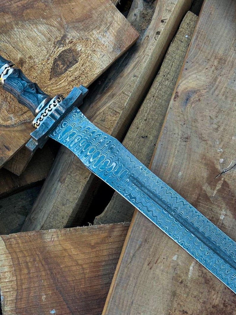 May include: A detailed image of a sword with a patterned blade and a dark wooden handle. The handle is adorned with silver and gold accents. The sword rests on a pile of wooden planks, showcasing the craftsmanship.