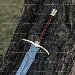 May include: A detailed image of a sword with a patterned steel blade and a brown leather-wrapped handle. The hilt and pommel are gold-colored. The sword is resting against a textured tree trunk. The text "RAGNAROK CRAFTED" is visible.