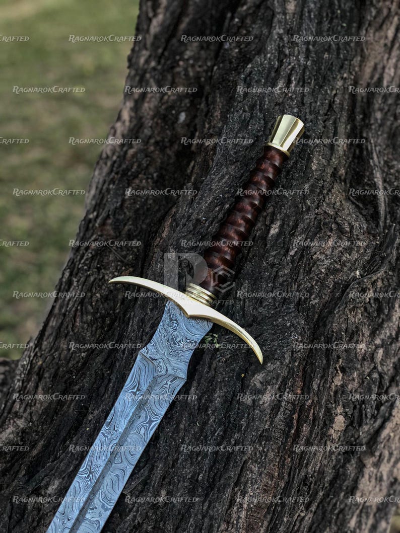 May include: A detailed image of a sword with a patterned steel blade and a brown leather-wrapped handle. The hilt and pommel are gold-colored. The sword is resting against a textured tree trunk. The text "RAGNAROK CRAFTED" is visible.