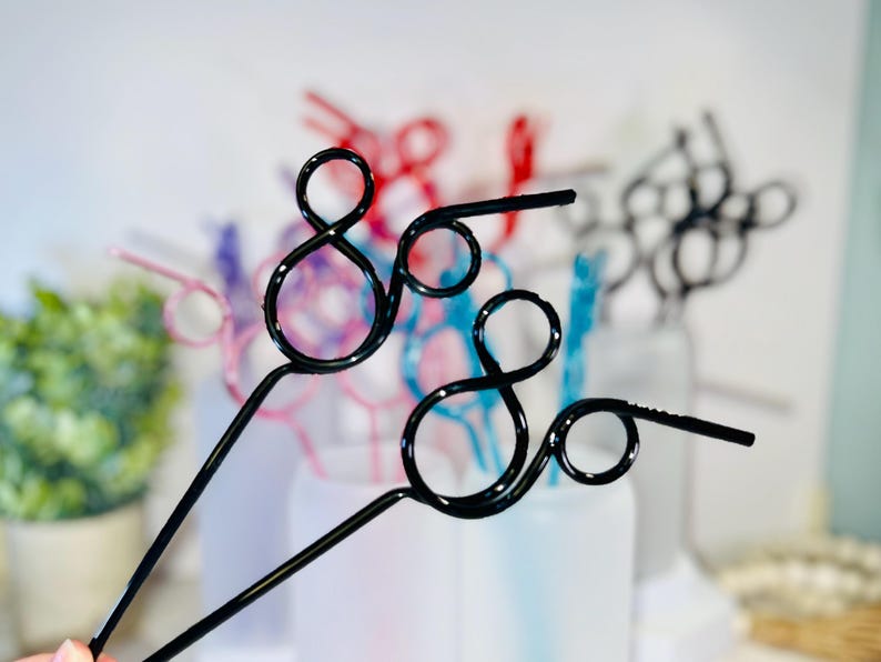 May include: Black metal decorative straws with a unique looped design. The straws are in focus, with other colorful straws in the background. The straws are a fun and stylish alternative to traditional straws.
