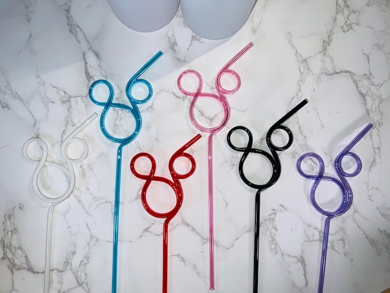 May include: A collection of colorful, reusable straws in various shades, including white, blue, red, pink, black, and purple. Each straw features a Mickey Mouse-inspired design. The straws are made of a clear, bendable material.