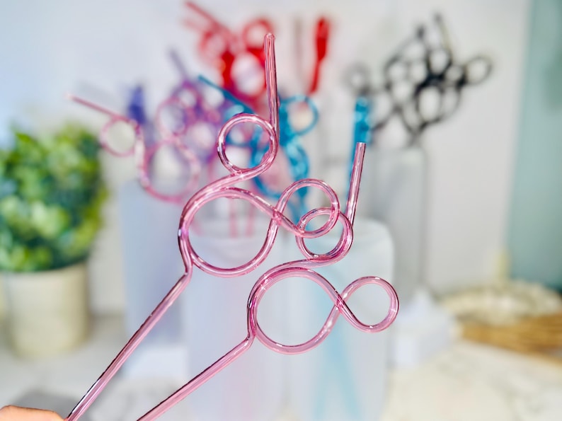 May include: Pink metal drink stirrers with a looped design. Other colorful stirrers in red, blue, and black are visible in the background. The stirrers are designed for beverages and add a decorative touch.