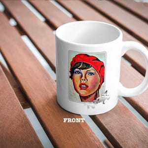 May include: White ceramic mug featuring a colourful illustration of a woman wearing a red beret. The woman has brown hair and brown eyes. The illustration is in a cartoon style.