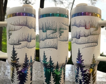 May include: Three stainless steel tumblers with a white background and a design of a forest with a starry sky. The tumblers have a rainbow iridescent finish.