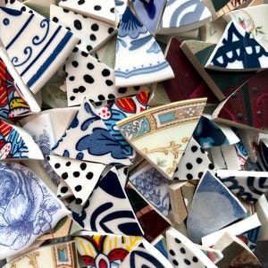 May include: A collection of broken ceramic pieces with various patterns and colors. The fragments feature designs in blue, white, and black, including polka dots, floral motifs, and geometric shapes. Some pieces have gold trim.