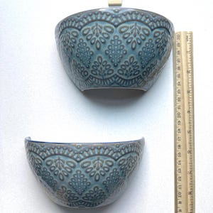 May include: Two blue ceramic bowls with a decorative embossed pattern. The bowls are approximately 6 inches wide and 3 inches tall. The bowls have a half-moon shape and are suitable for decorative or functional use.