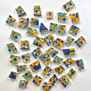 May include: A collection of colorful, patterned tiles scattered on a white surface. The tiles feature a floral design with blue, yellow, orange, and red hues. Two wooden letter tiles, one with the letter "T", are also present.
