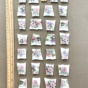 May include: Scattered pieces of a broken porcelain teacup, each with a floral design in pink, purple, and green. A wooden ruler with inch markings and a wooden letter tile are also present.