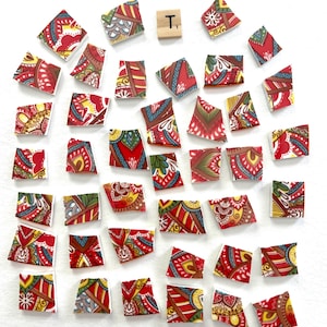 May include: A collection of forty-one irregular ceramic mosaic tiles featuring intricate red, yellow, green, and blue patterns, arranged alongside a single square wooden tile displaying the letter T and the number 1 in black ink.