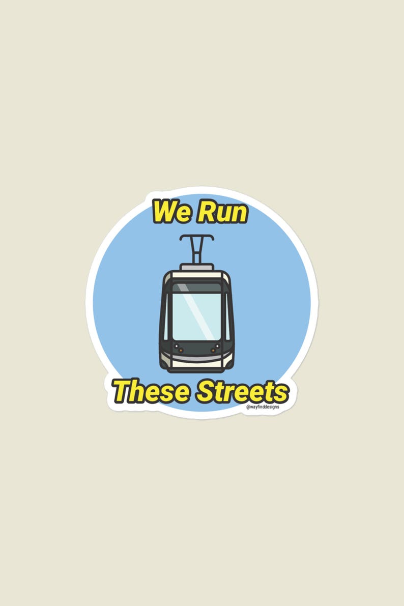 May include: A sticker featuring a cartoon tram in black, gray, and white, set against a light blue circle. The text "We Run These Streets" is in yellow and black. The design is simple and modern, suitable for urban transit enthusiasts.