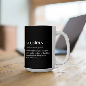 以下が含まれることがあります： 黒い背景に白い文字で「seesters /sea-sturs/ noun/plural the uncanny way you and your sister can be texting or thinking the exact same thing at the exact same time.」と書かれた白いセラミックマグカップ