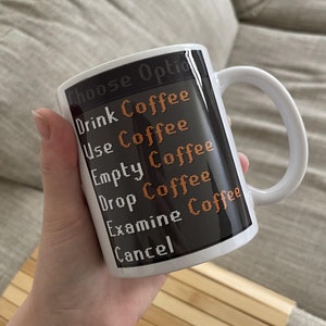 Pode incluir: Uma caneca de cerâmica branca com fundo preto e texto laranja que diz "Choose Option", "Drink Coffee", "Use Coffee", "Empty Coffee", "Drop Coffee", "Examine Coffee" e "Cancel".