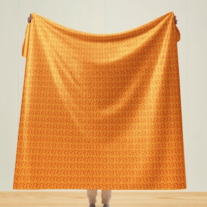 May include: A person holding up a yellow blanket with a red floral pattern. The blanket is made of a soft, comfortable material and is perfect for snuggling up on the couch.