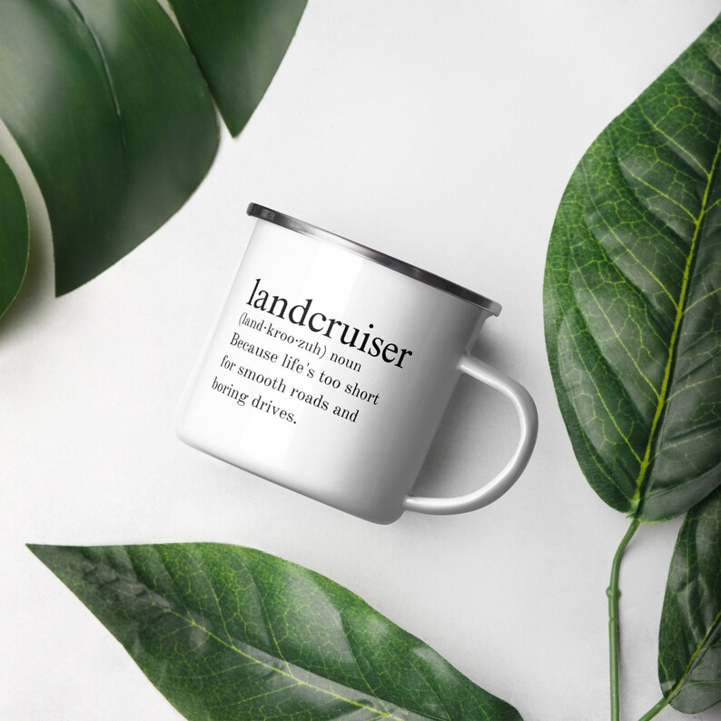 May include: White enamel camping mug with black text that reads "landcruiser (land-kroo-zuh) noun Because life's too short for smooth roads and boring drives."