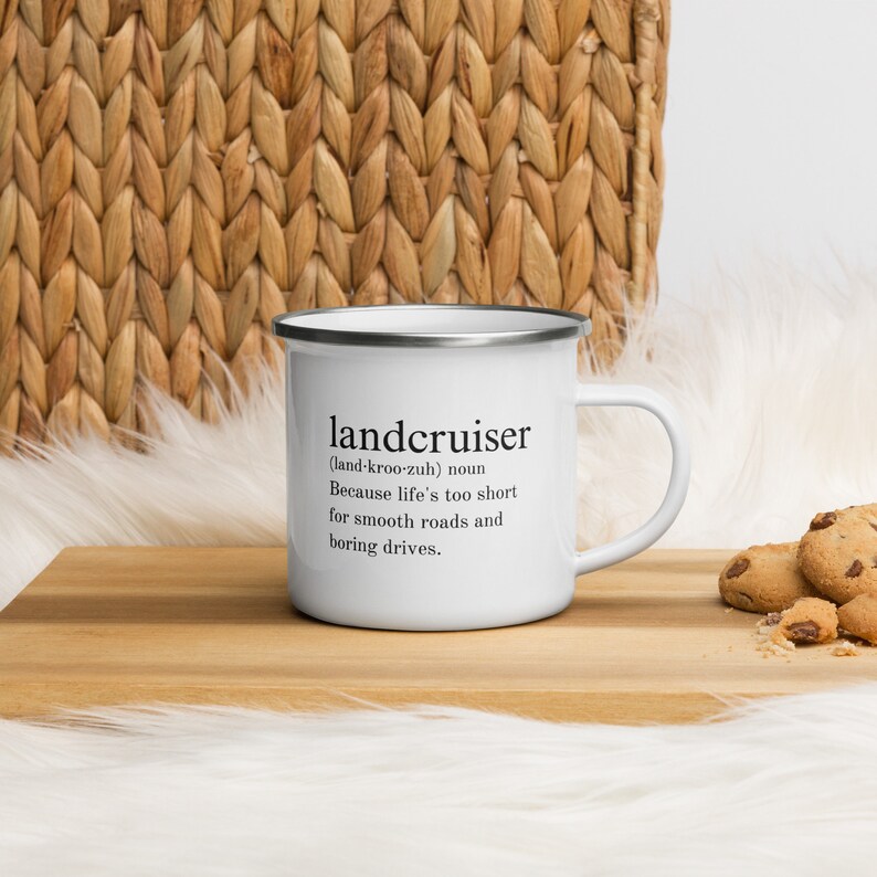 May include: White enamel mug with a black and silver rim. The mug has a black text graphic that reads "landcruiser (land-kroo-zuh) noun Because life's too short for smooth roads and boring drives."