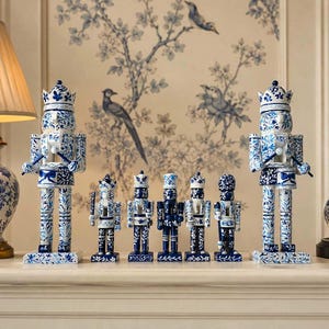 May include: A collection of seven decorative nutcracker figurines featuring a consistent blue and white floral pattern. The set includes two large nutcrackers with crowns and five smaller figures of varying designs, all standing on rectangular bases.