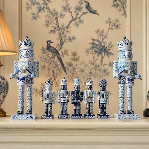 May include: A set of seven nutcracker figurines featuring a white and blue floral pattern. The two larger nutcrackers stand on the ends, while five smaller nutcrackers are arranged in the center, all displaying intricate blue painted details.