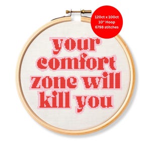 May include: A cross-stitch embroidery hoop with the text "your comfort zone will kill you" in red. The hoop is 10 inches in diameter and has 6798 stitches. The text is stitched on white fabric.