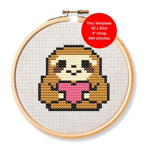 May include: A cross-stitch design of a sloth holding a pink heart, framed in a 10 cm embroidery hoop. The sloth is brown, beige, and black, with the text "Tiny Template" and stitch details on a red circle.