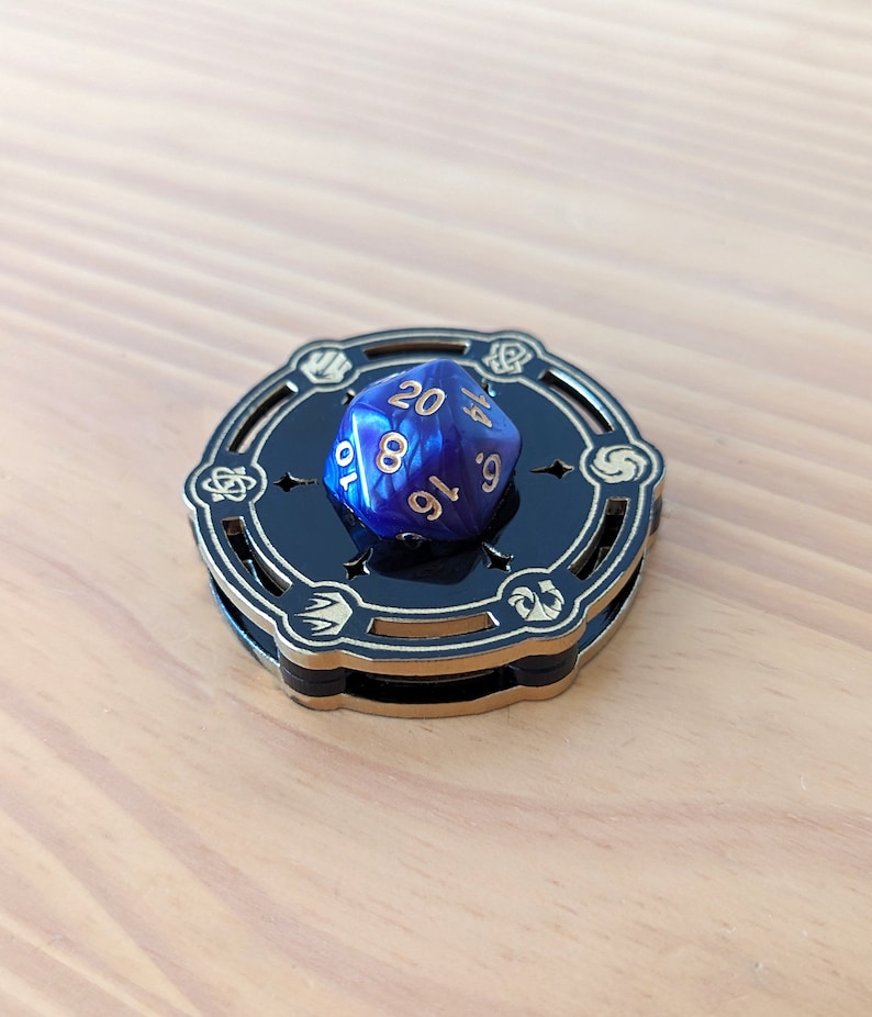 May include: A blue and gold dice tower with a blue 20-sided die resting on top. The die has the numbers 10, 8, 16, 9, 4, and 20 visible.