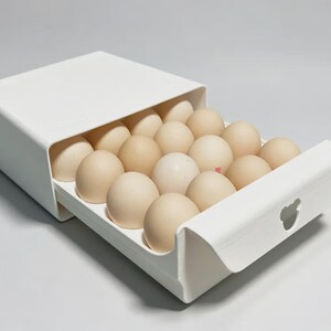 May include: A white plastic egg storage drawer featuring a sliding tray design with a small bear-shaped cutout handle. The container holds eighteen light brown eggs arranged in a grid, providing a compact and organized solution for refrigerator storage.