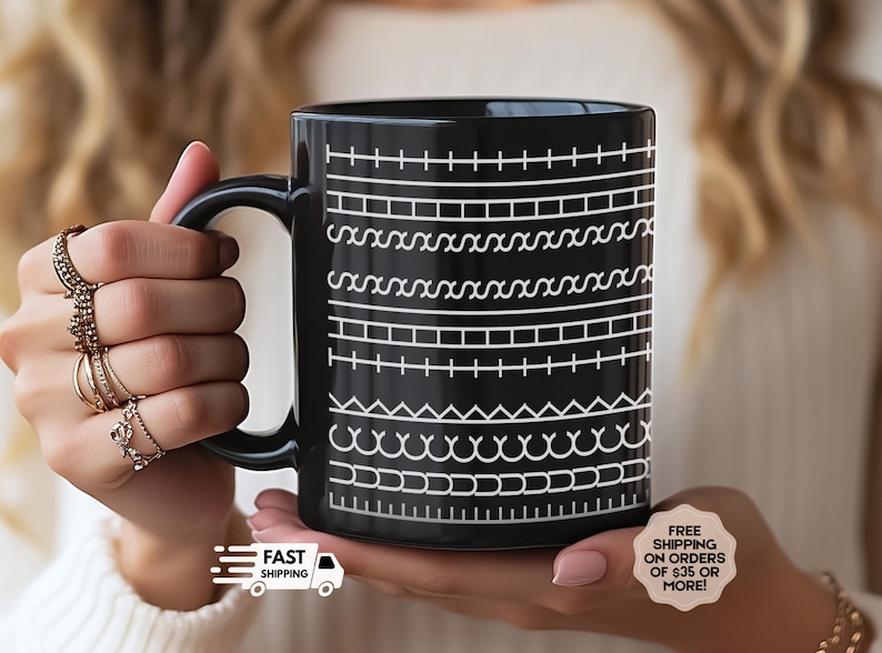 K&ouml;nnte beinhalten: Schwarze Keramik-Tasse mit wei&szlig;em geometrischen Muster. Das Design zeigt verschiedene horizontale Linien mit Formen wie Quadraten, Zickzacklinien und Kurven. Die Tasse wird in den H&auml;nden einer Person gehalten.