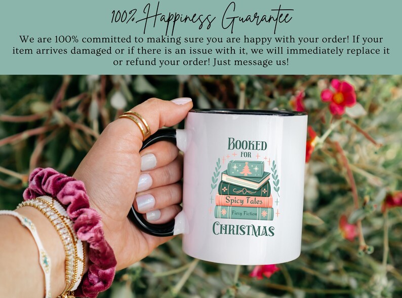May include: White ceramic mug with a black rim and handle. The mug has a design of a stack of books with the text "Booked for Christmas" and "Spicy Tales" on the books. The mug is being held by a hand.