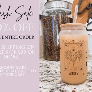 K&ouml;nnte beinhalten: Ein gefrosteter Glasbecher mit einem braunen Holzdeckel und einem Strohhalm. Der Becher hat ein schwarz-wei&szlig;es Design mit einem astrologischen Symbol, dem Text "ARIES" und dem Namen "ASHLEY".