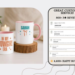 May include: Two white ceramic mugs with pink interiors and handles. One mug has "IN MY SHOWGIRL ERA" in orange text. The other mug has "SARAH" in teal with a bow graphic. Both mugs sit on a wooden coaster.
