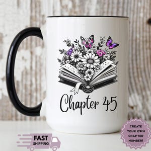 May include: White ceramic mug with a black handle and rim. The mug features a floral design with daisies, purple and pink flowers, and butterflies above an open book. The text "Chapter 45" is written in black.