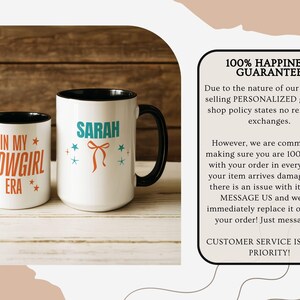 May include: Two white ceramic mugs with black handles and rims. One mug has "IN MY SHOWGIRL ERA" in orange and red text. The other mug has the name "SARAH" in teal, with a bow and star accents. Both mugs are on a light wood surface.