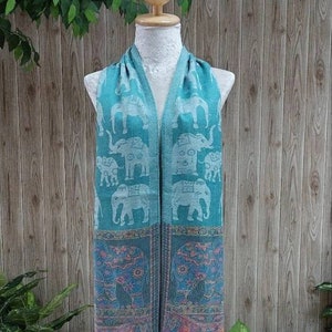 May include: A teal blue scarf with a white elephant pattern. The scarf has a fringe border and is displayed on a mannequin.