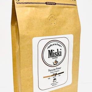 Może przedstawiać: Brązowa papierowa torba z zamkiem błyskawicznym i białą etykietą, na kt&oacute;rej widnieje napis "Quality at its Finest. Miski Coffee" i "Peruvian Primor". Etykieta zawiera r&oacute;wnież wskaźnik stopnia palenia z czarną linią wskazującą średnie palenie.