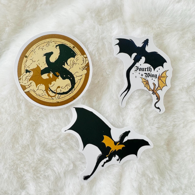 May include: Three sticker designs featuring dragons. The first sticker is a round sticker with a gold background and a black dragon with a yellow dragon inside. The second sticker is a black dragon with a yellow dragon inside and the text "Fourth Wing". The third sticker is a black dragon with a yellow dragon inside.
