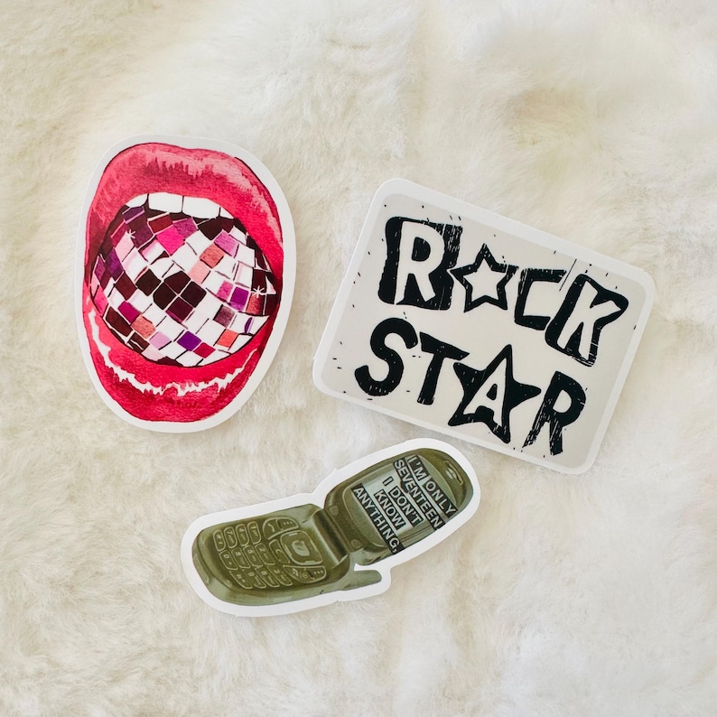 May include: Three stickers: one featuring a pair of bright red lips biting into a multi-colored disco ball, a rectangular sticker with the black text ROCK STAR, and a green flip phone sticker with the text I'M ONLY SEVENTEEN I DON'T KNOW ANYTHING.