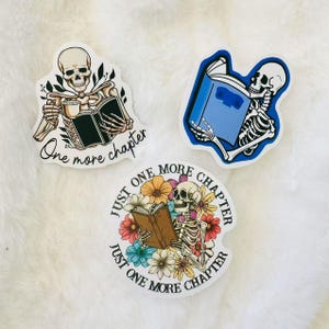 May include: Three skeleton stickers with the text "One more chapter" and "Just one more chapter" around them. The skeletons are reading books. One sticker has a blue book, one has a black book, and one has a brown book with flowers around it.
