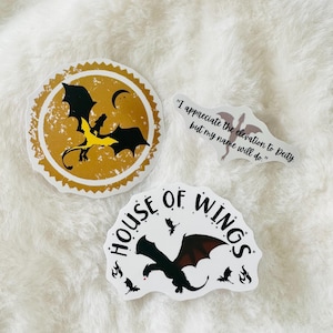 May include: Three stickers featuring dragons. One sticker is gold with a black dragon and the text "House of Wings". Another sticker is white with a black dragon and the text "I appreciate the elevation to Deity, but my name will do."