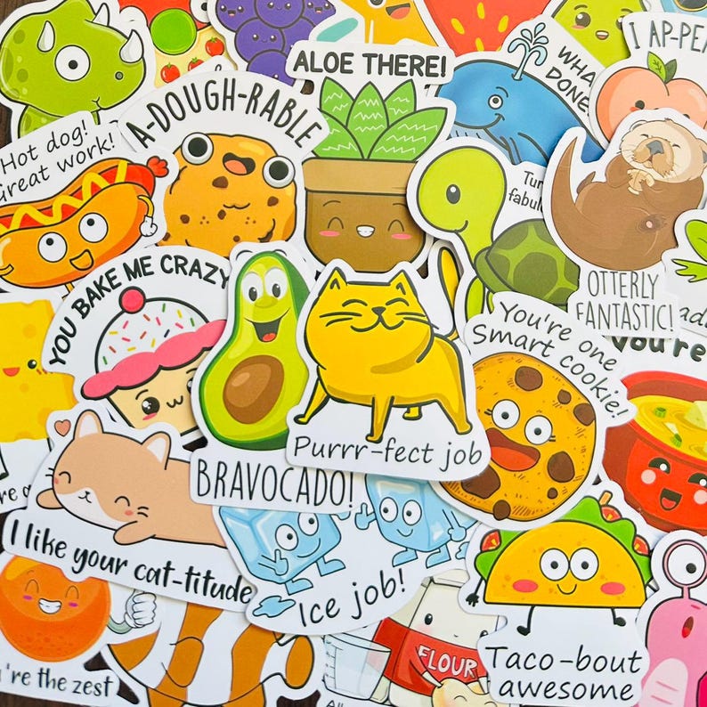 May include: A collection of colorful vinyl stickers featuring cartoon characters with puns, including a yellow cat with Purrrr-fect job, a cookie with You're one smart cookie, an avocado with Bravocado, a taco with Taco-bout awesome, and an aloe plant with Aloe there.
