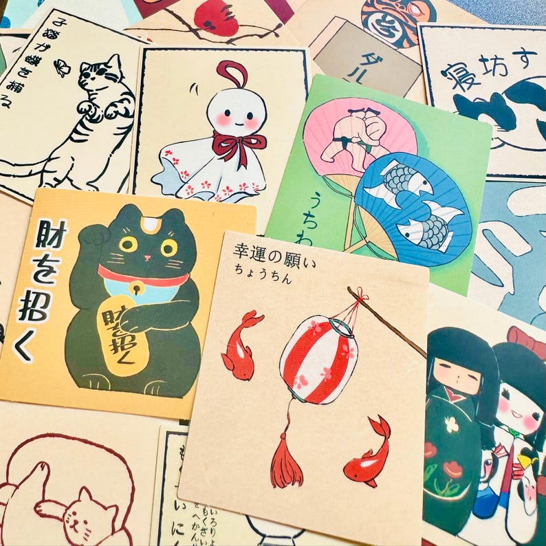 Op de afbeelding: Een verzameling kleurrijke Japanse kaarten met illustraties van katten, vissen, lantaarns en andere traditionele afbeeldingen. De kaarten bevatten Japanse tekst, waaronder "財を招く", wat vertaalt naar "rijkdom uitnodigen".