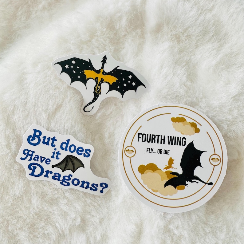 May include: Three stickers featuring dragons. One sticker has a black dragon with yellow accents and stars on its wings. Another sticker has a black dragon with a white background and the text "Fourth Wing Fly... or Die". The third sticker has a black dragon with blue text that reads "But does have it Dragons?".