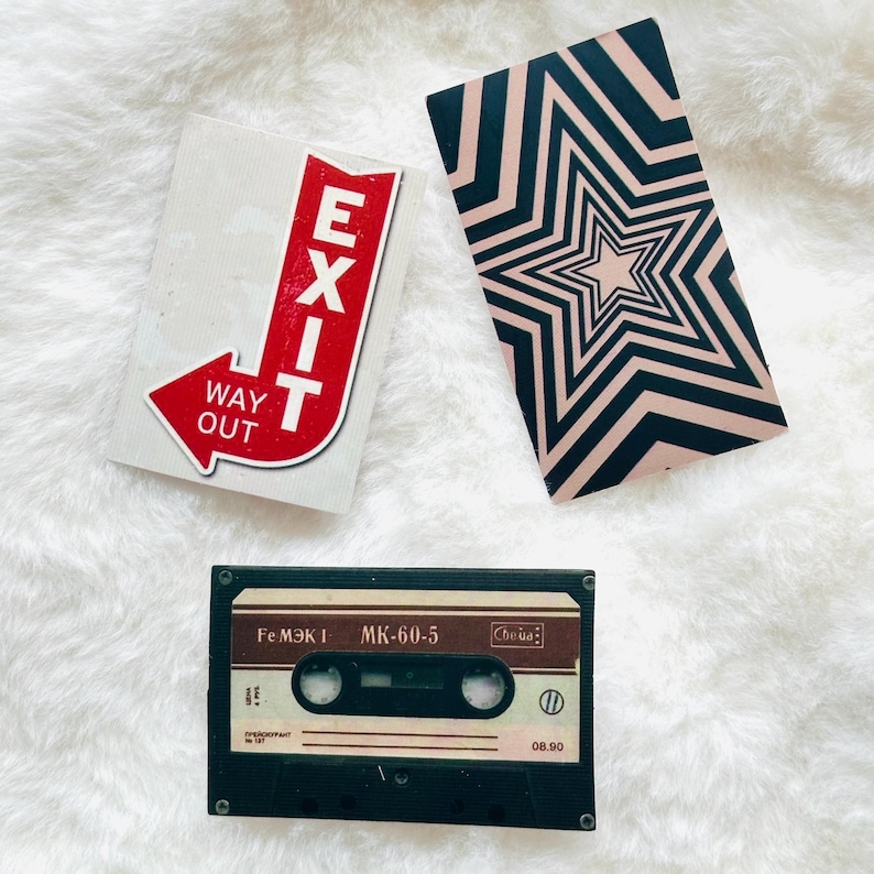 May include: A rectangular sticker featuring a red arrow with the white text EXIT WAY OUT, a rectangular card with a black and beige star pattern, and a black audio cassette tape labeled Fe MЭK I MK-60-5 with Cyrillic text and numerical markings.