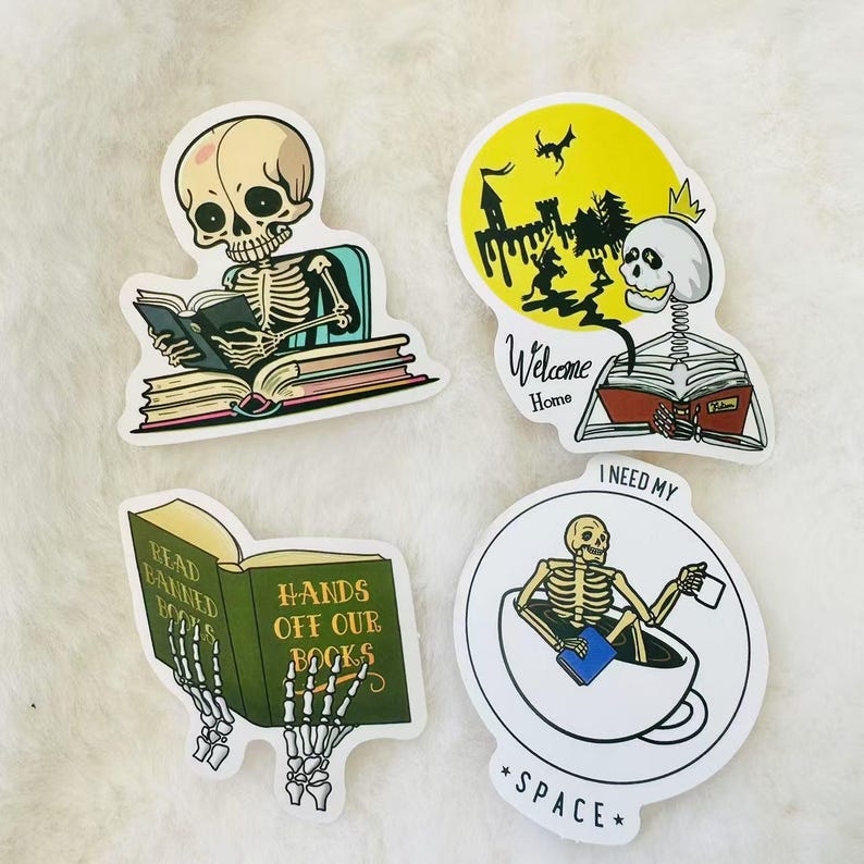 May include: Four skeleton themed stickers with different designs. One sticker features a skeleton reading a book with the text "Read Banned Books". Another sticker features a skeleton reading a book with the text "Hands Off Our Books". A third sticker features a skeleton sitting in a cup with the text "I Need My Space". The final sticker features a skeleton reading a book with the text "Welcome Home".