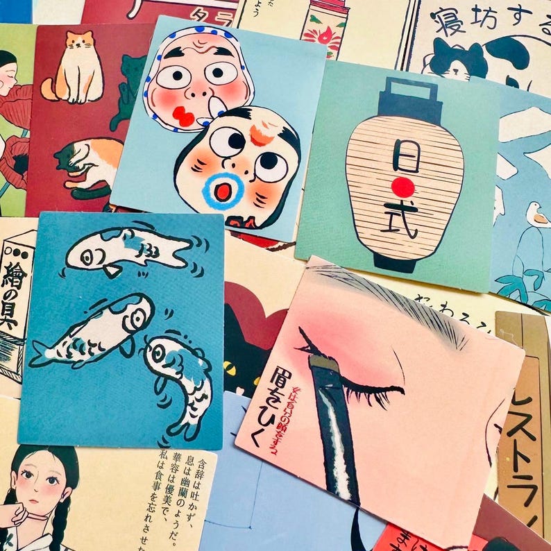 Op de afbeelding: Een verzameling kleurrijke Japanse illustraties gedrukt op papieren kaarten. De kaarten bevatten afbeeldingen van vissen, een lantaarn, een gezichtsmasker en een kat. De tekst op de kaarten is in het Japans.