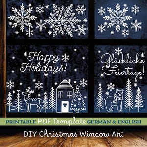 May include: White snowflake and holiday-themed window art. The design includes snowflakes, a house, trees, a deer, and the text "Happy Holidays!" and "Gl&uuml;ckliche Feiertage!" on a dark blue background. DIY Christmas Window Art.