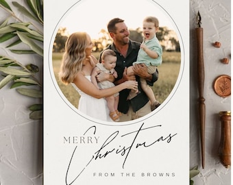 May include: A Christmas card with a photo of a family of four. The parents are holding their two young children. The card has a black circle around the photo and the text "Merry Christmas from the Browns" in black script.