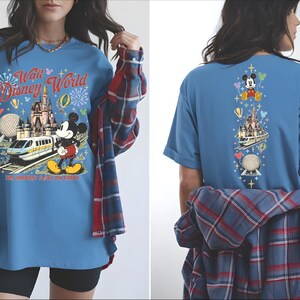 A woman wearing a blue t-shirt with a Disney World-themed design, including Mickey Mouse and various Disney landmarks.